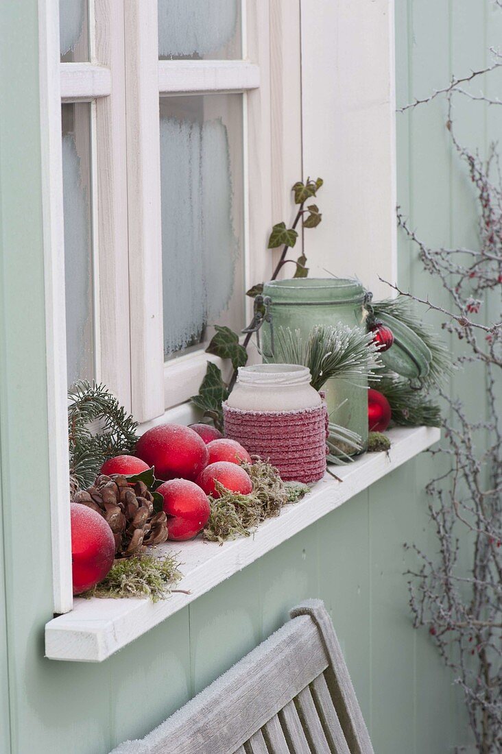 Windowsill decorated with red balls, lanterns, cones, moss, ivy
