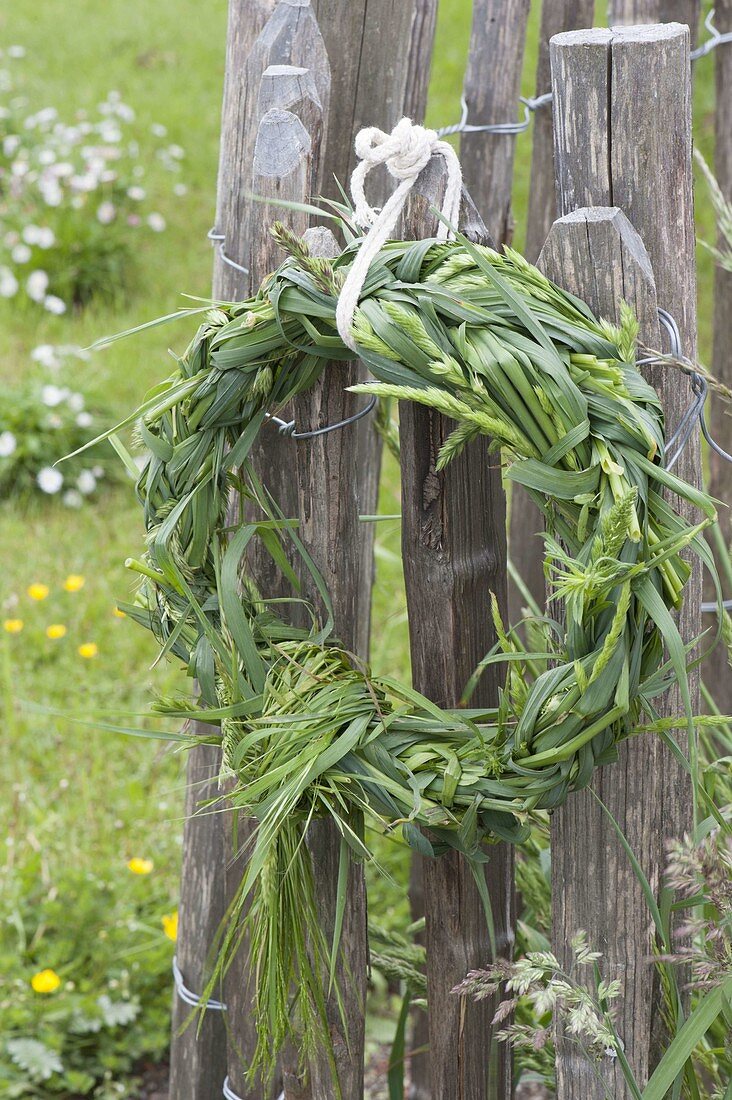 Wild flowers bouquet, wreath woven from grasses, hung on a fence