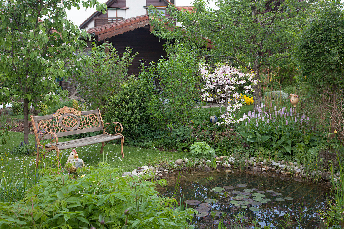 Romantischer Frühlingsgarten mit Bank am Teich