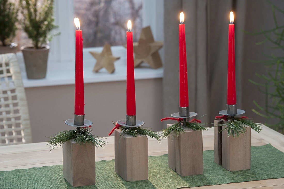 Moderner Adventskranz aus Kerzenhaltern auf Holz-Kloetzen, roten Kerzen