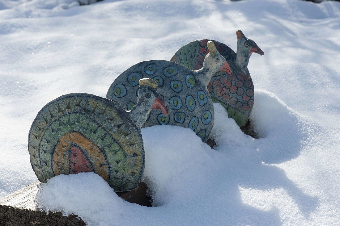 Ceramic peacocks on wooden beams on the snow