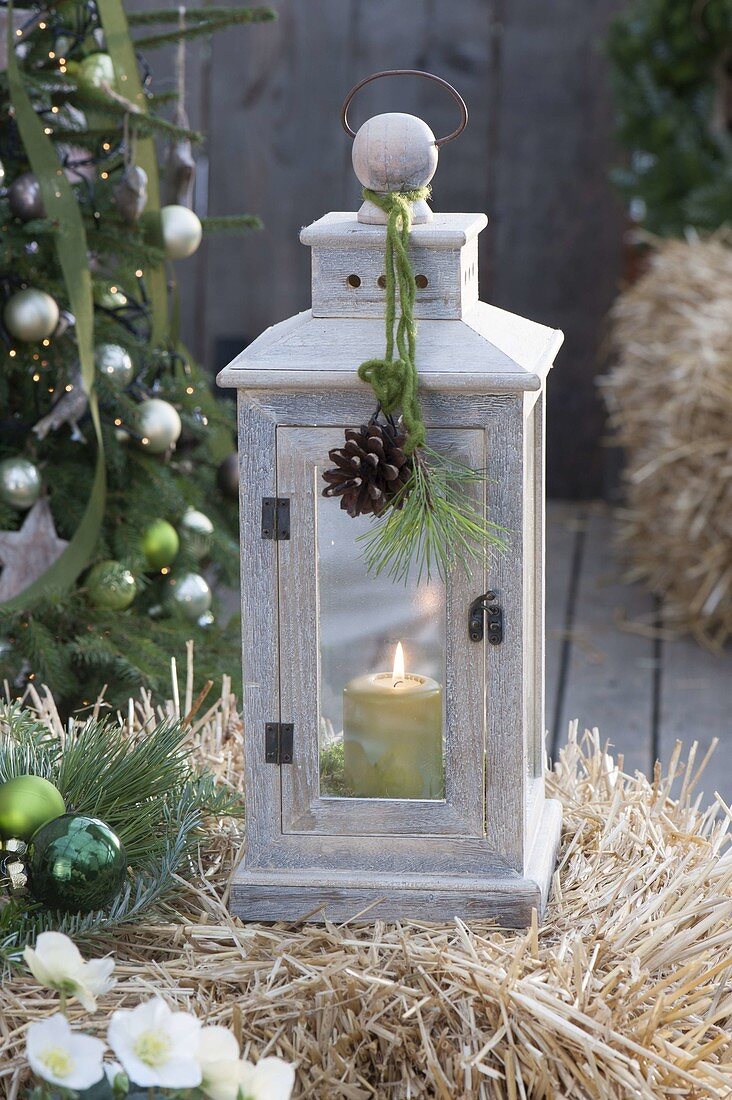 Wooden lantern with green candle on straw bales