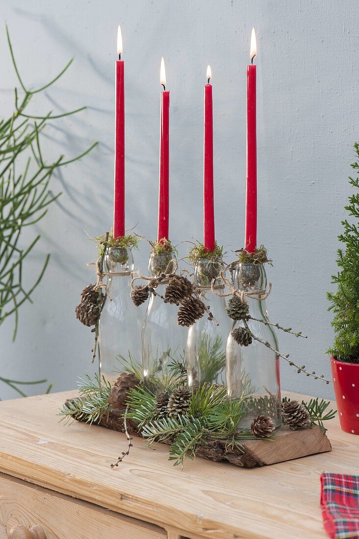 Red stick candles with moss placed on bottles as a candle holder