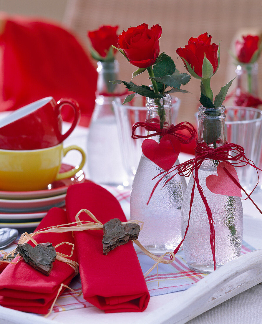 Rosa / rote Rosen in Glasflaschen mit Herzen aus Pappe