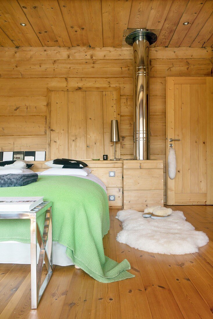Gemütliches Schlafzimmer in Datcha mit Edelstahl-Ofenrohr und weißem Schaffell als Bettvorleger