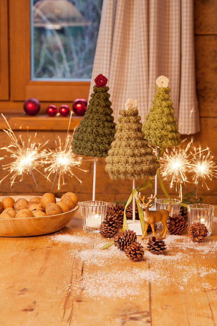 Tiny crocheted Christmas trees and sparklers on wooden table