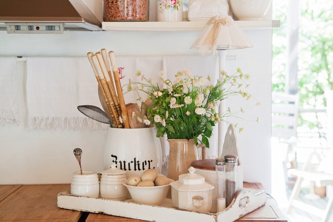 Küchenutensilien, Zuckerdosen und Blumenstrauss auf weißem Holztablett