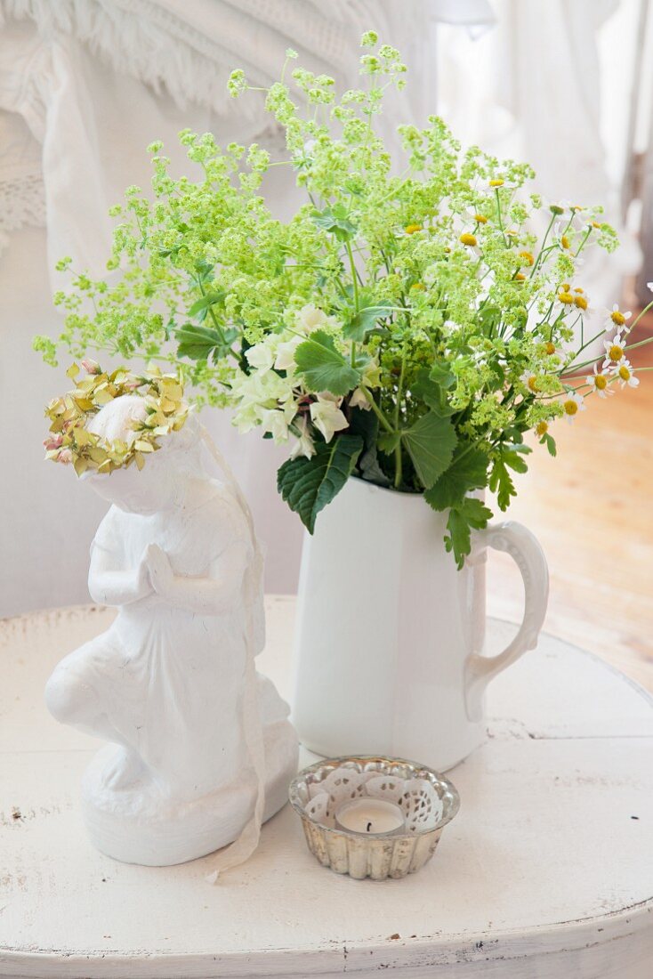 weiße Krugvase mit Blume, Windlicht und Porzellanfigur auf Tisch