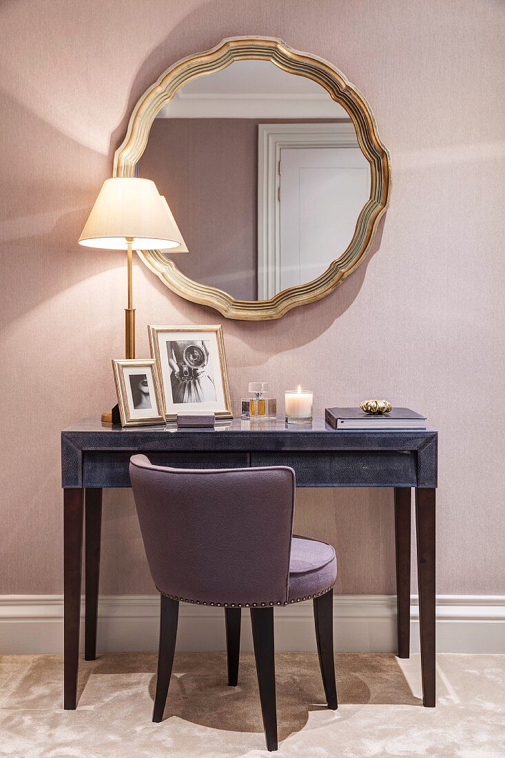 Upholstered chair at console table below round mirror