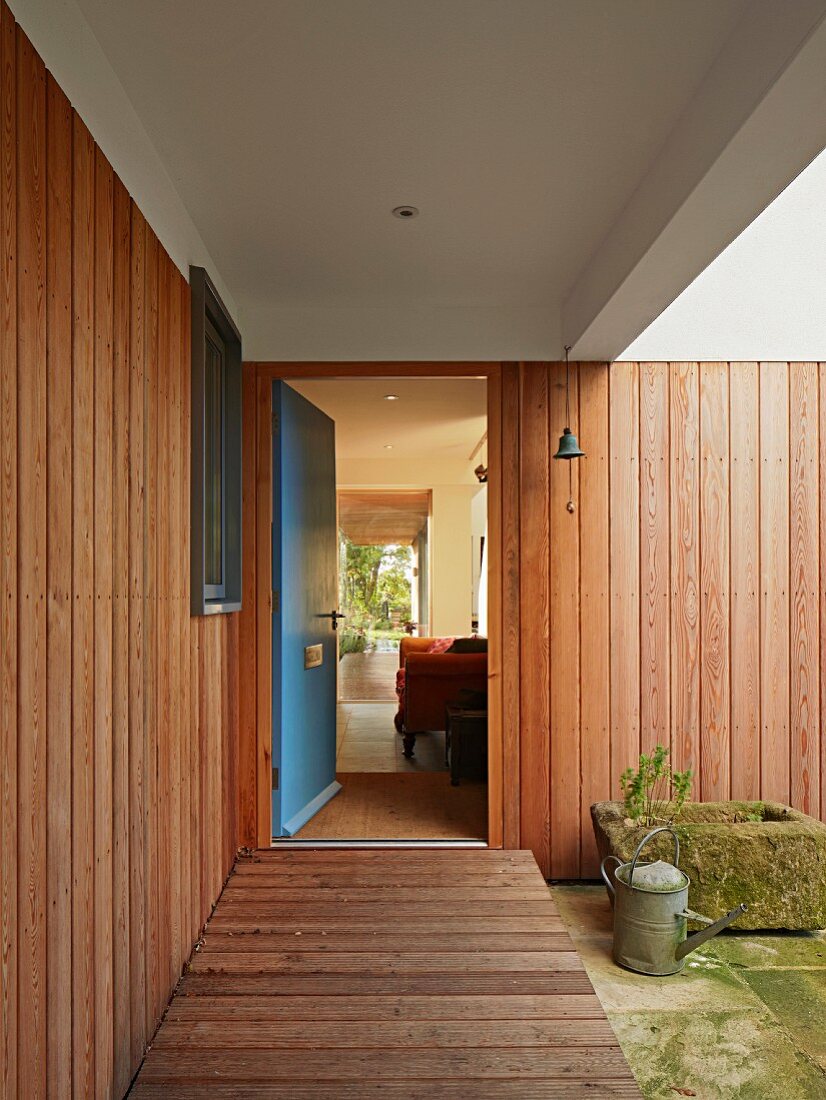 Offene, blaue Haustür zu einem Haus mit Holzverkleidung