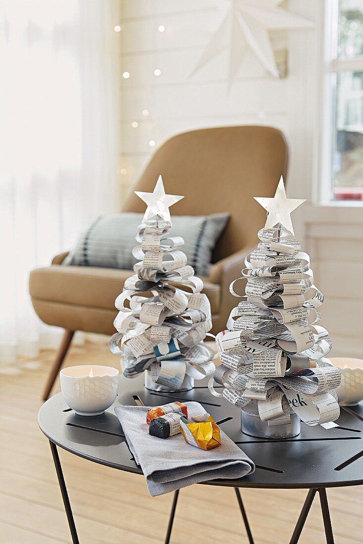 Kleine Weihnachtsbäume aus Zeitungspapier auf einem Tischchen