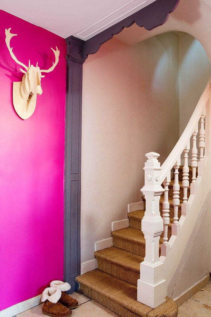 Pinkfarbene Wand mit Dekotrophäe vor Holztreppenaufgang