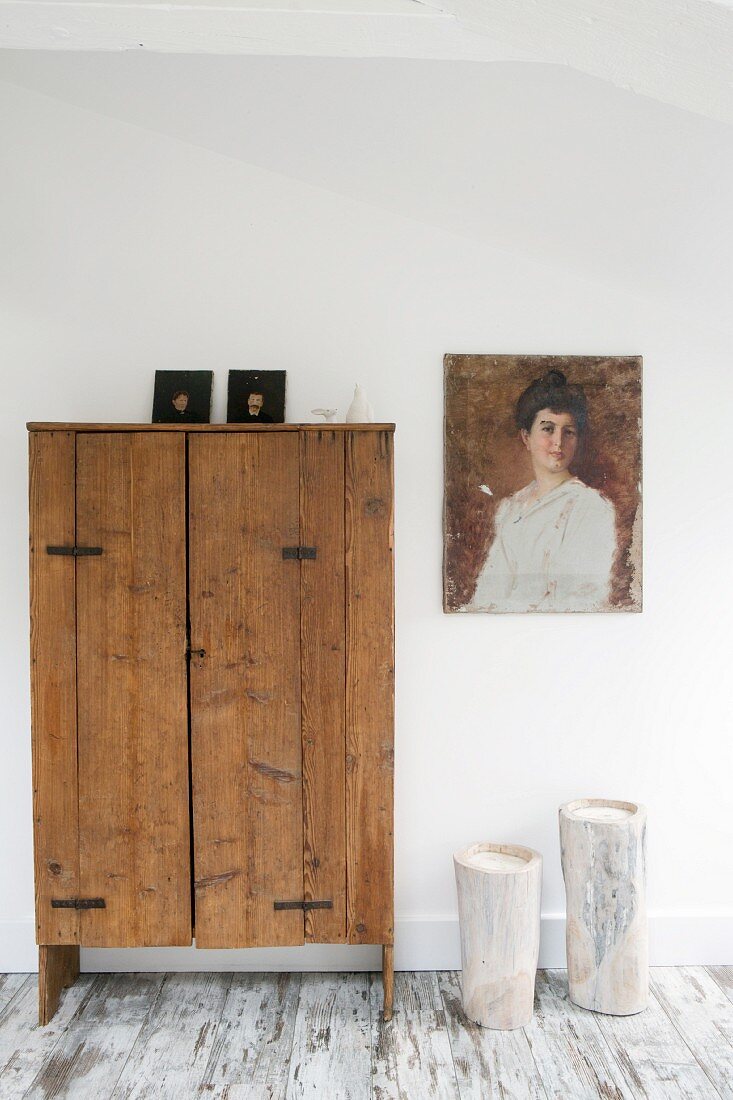 Painting of woman and candles in hollow tree trunks next to rustic wooden cupboard