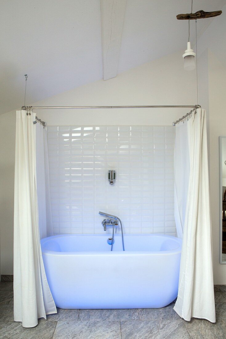 White bathtub with shower curtain bathed in blue light in renovated period building