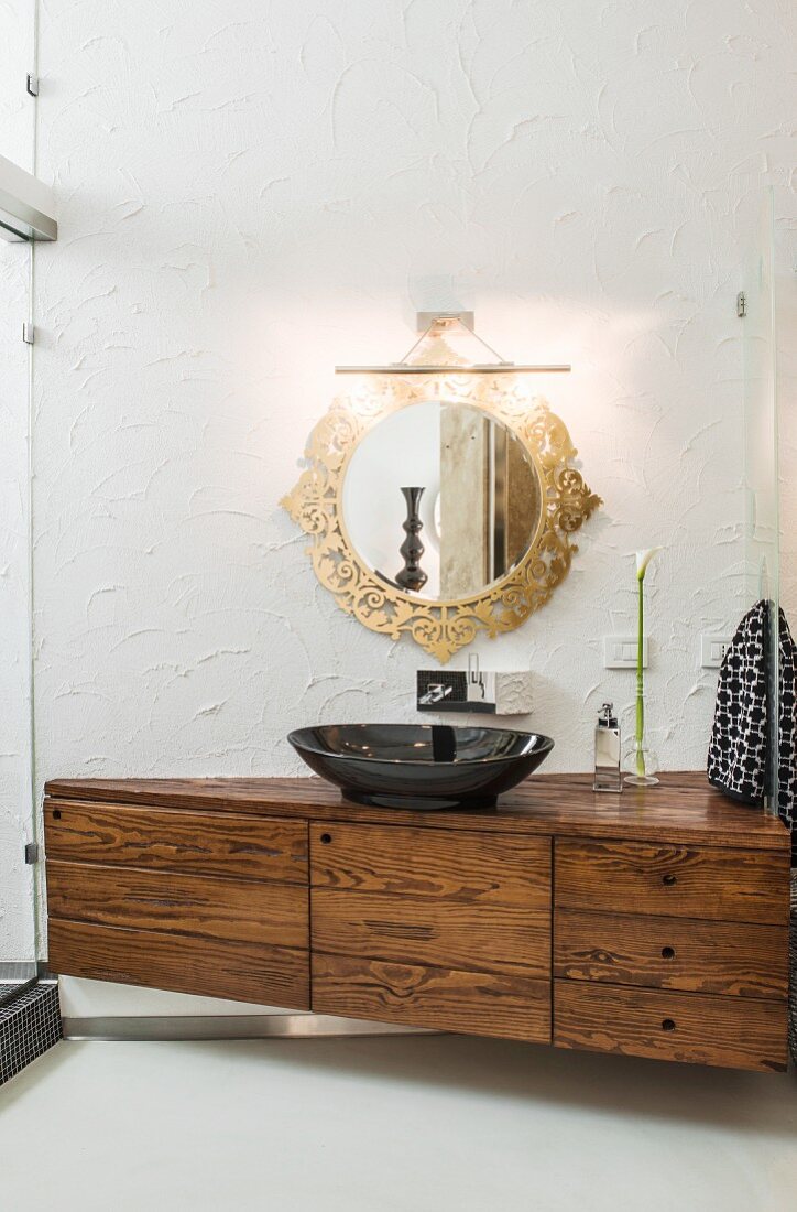 Elegantes Waschtischmöbel mit schwarzem Waschbecken und runder Spiegel mit verziertem goldfarbenem Rahmen