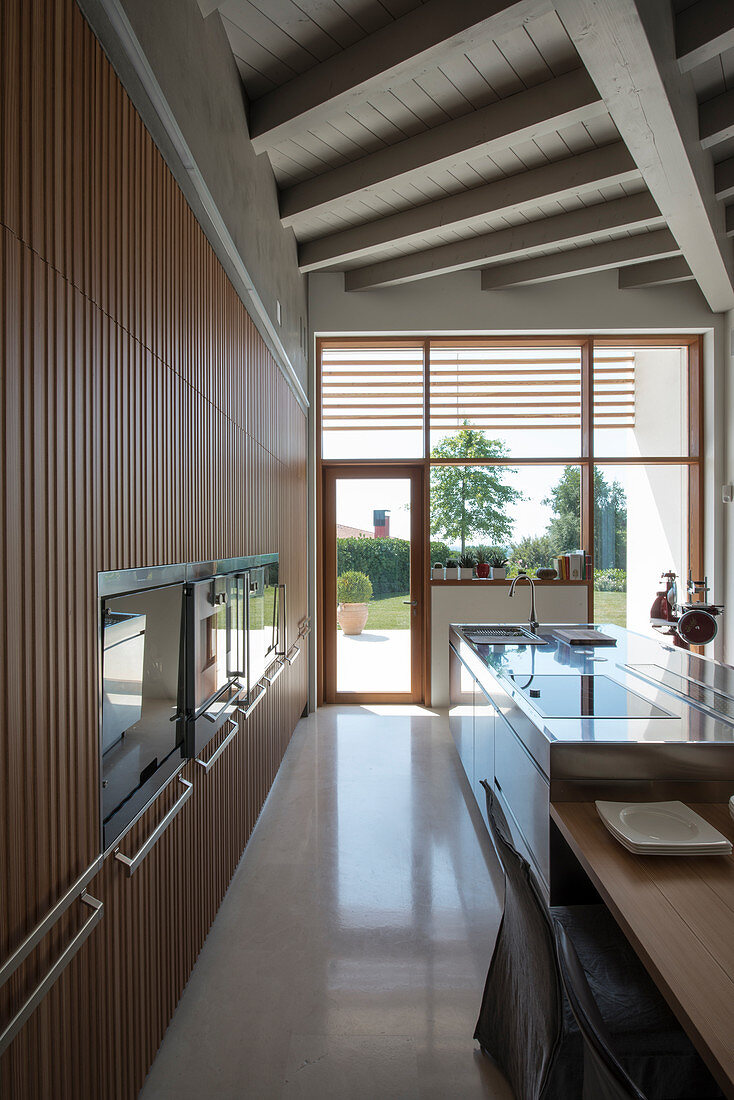 Designerküche mit Einbaugeräten und Mittelblock, im Hintergrund Terrassenzugang