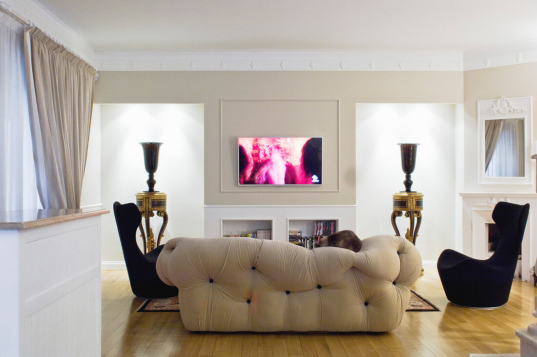 Designer seating in front of urns on tables in niches with indirect lighting in elegant living room