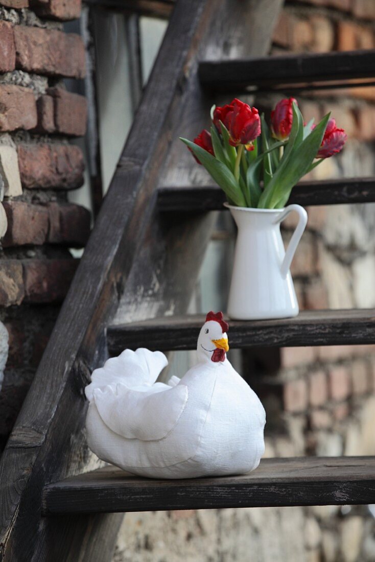DIY-Henne aus Stoff und Tulpen in weißem Krug auf rustikaler Holztreppe