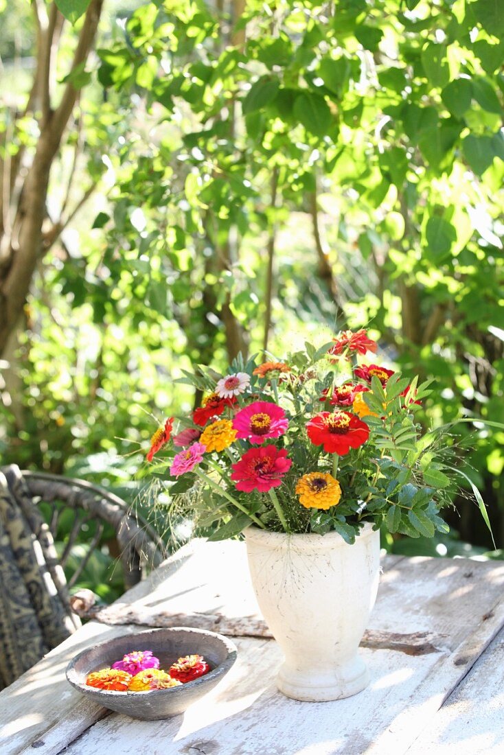 Strauss aus Zinnien, Gräsern und Wildrosenzweigen in schlichter Vase auf Gartentisch