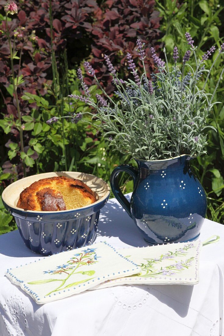 DIY-Topflappen und Keramikgefässe mit Kuchen und Lavendel auf weiß gedecktem Gartentischchen
