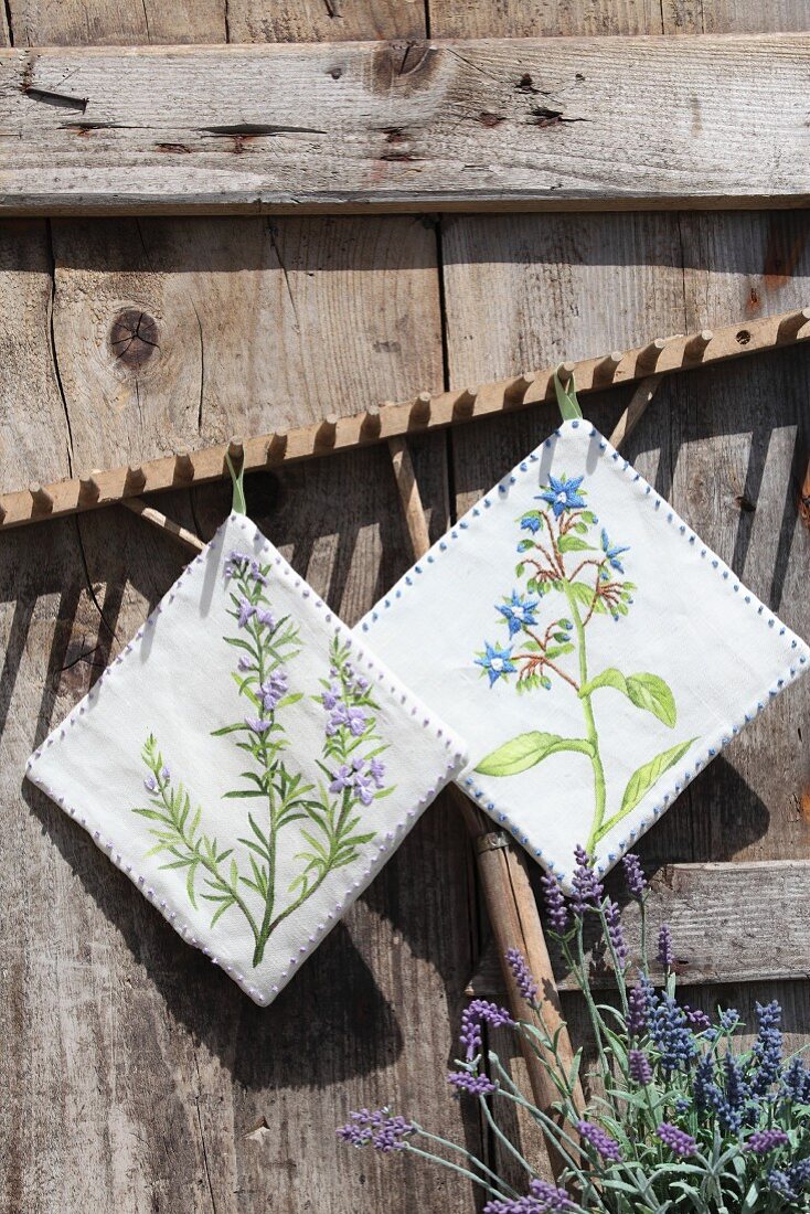 Hand-made pot holders with floral motifs run from wooden rake against rustic wooden wall