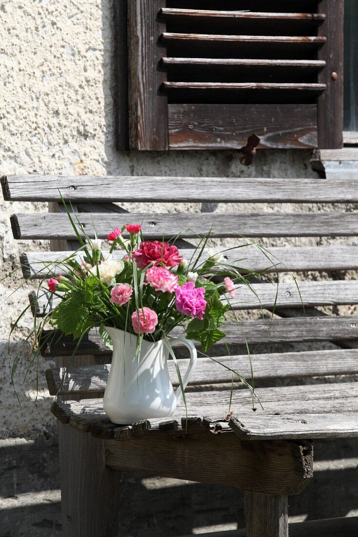 Posies of carnations in jug on weathered garden bench