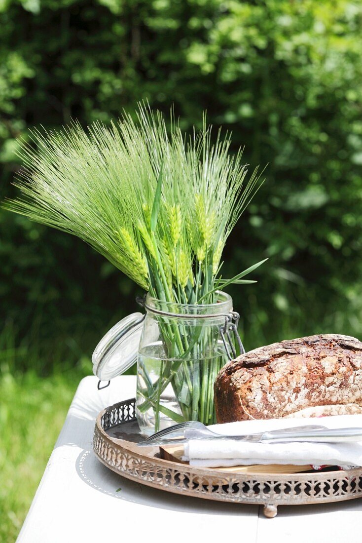 Gerstenähren im Einmachglas auf dem Tablett mit Brot