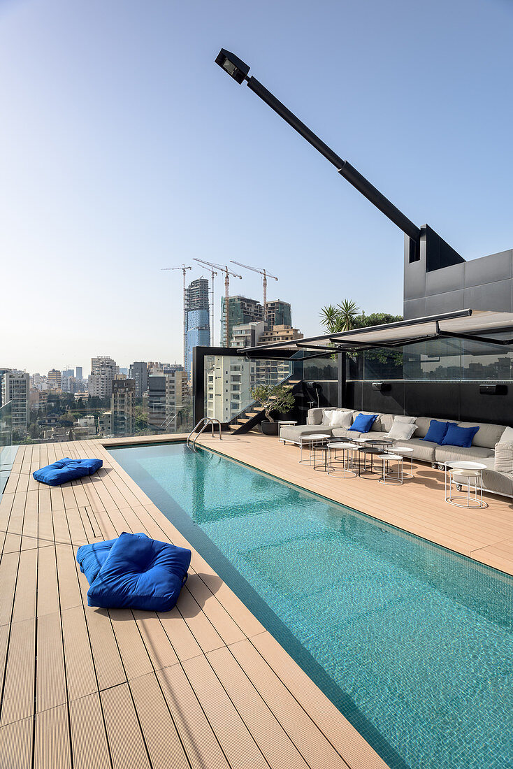 Long, narrow swimming pool and sofa combination on roof terrace with view of city