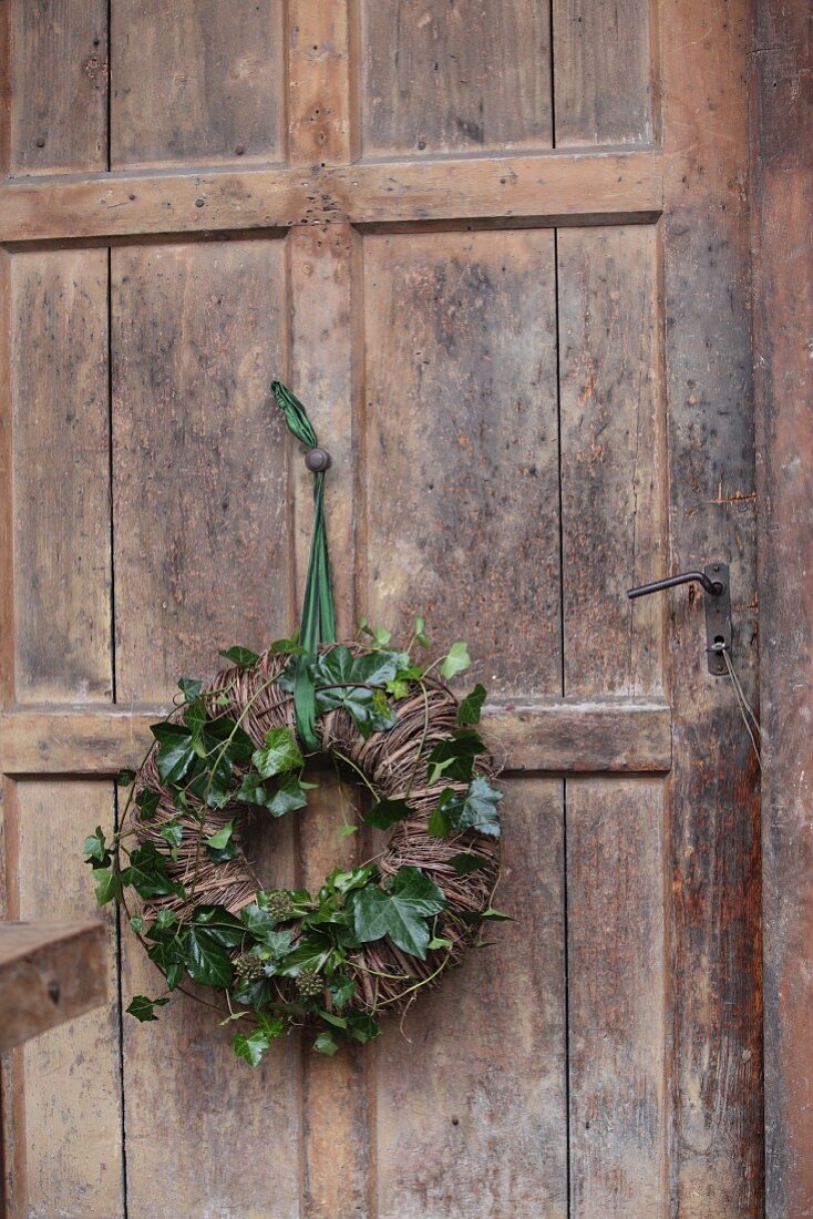 Wreath of willow and green ivy tendrils hung on rustic wooden door