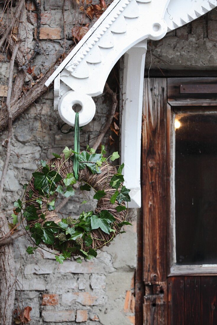 Weidenkranz mit grünen Efeuranken an weißem Vordach aufgehängt