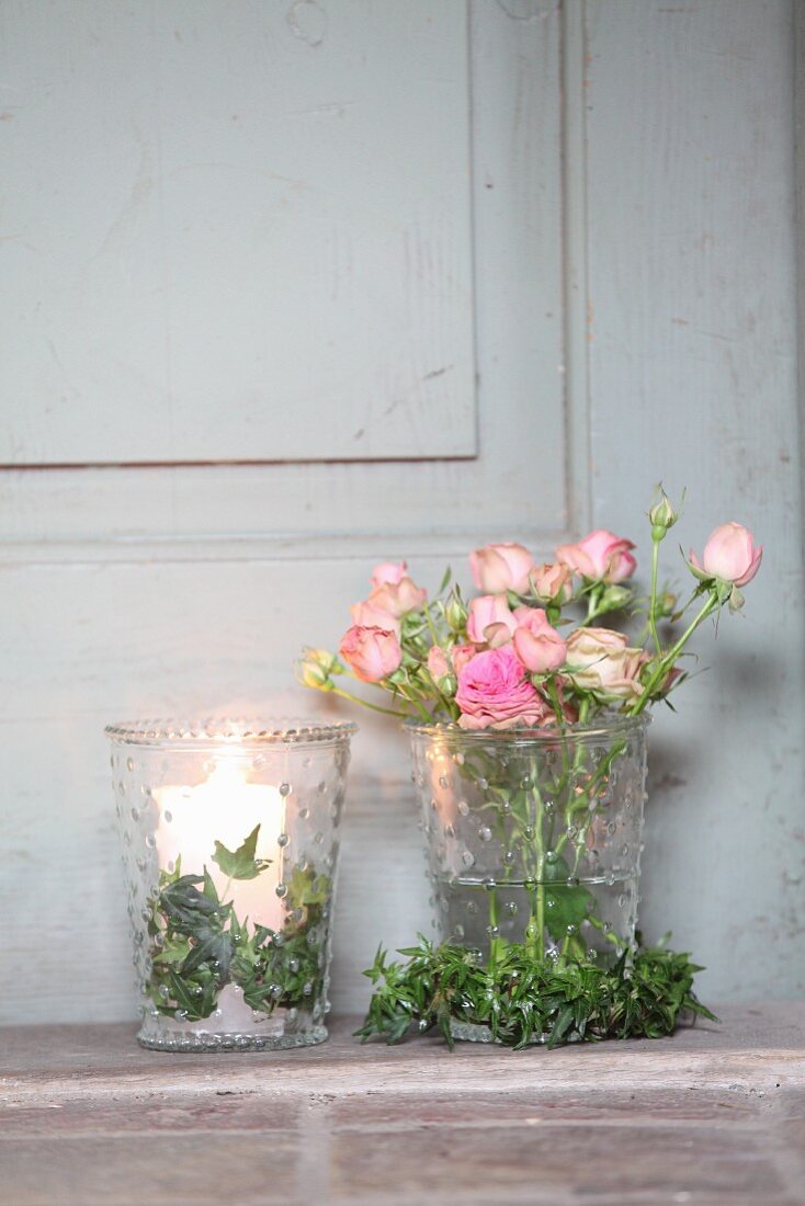 Romantic arrangement of ivy wreaths, roses and lit candles in glass vases
