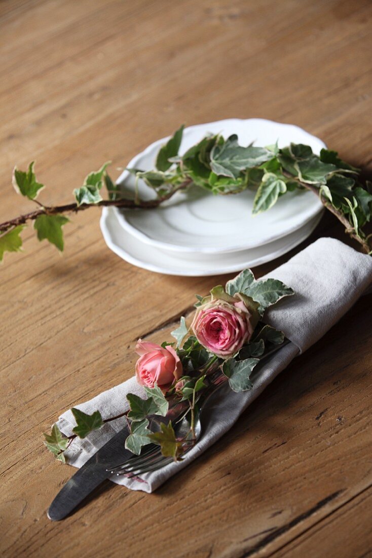 Romantische Tischdekoration mit Rosenblüten und Efeu in Stoffserviette mit Besteck