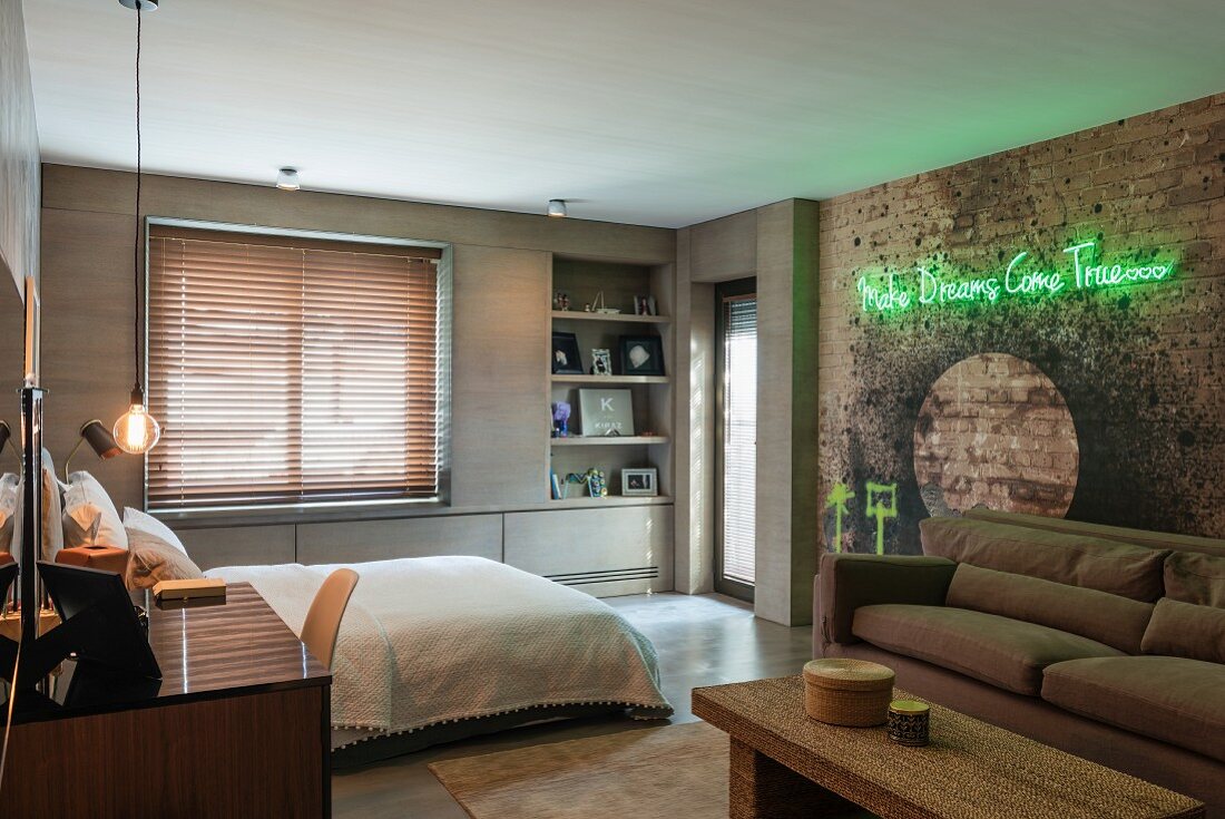 Schlafzimmer mit brauner Couch vor rustikaler Ziegelwand mit künstlerischer Gestaltung und grüner Leuchtschrift