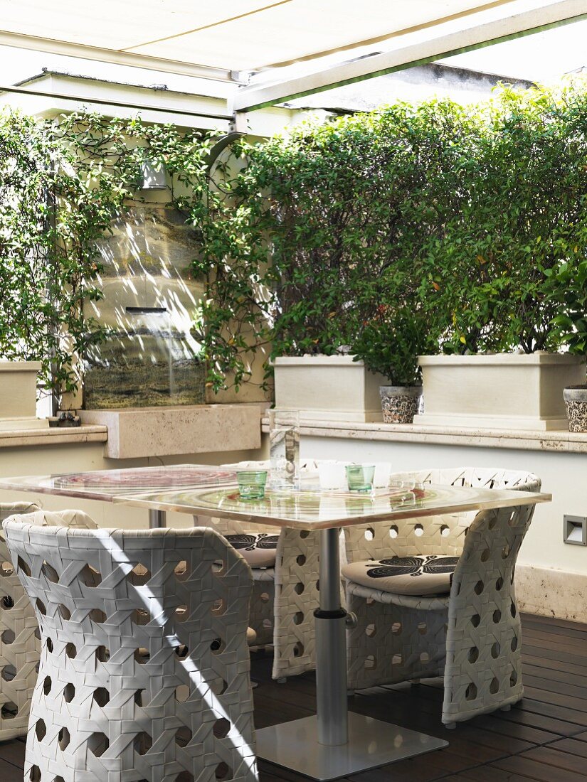 Geschützte Terrasse mit Gartentisch und geflochtenen Outdoorstühlen