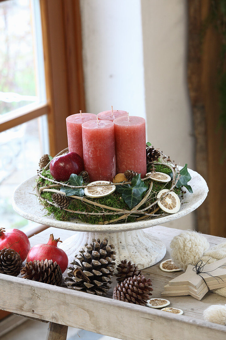 Rustikaler Adventskranz mit roten Kerzen auf einem Tortenfuß