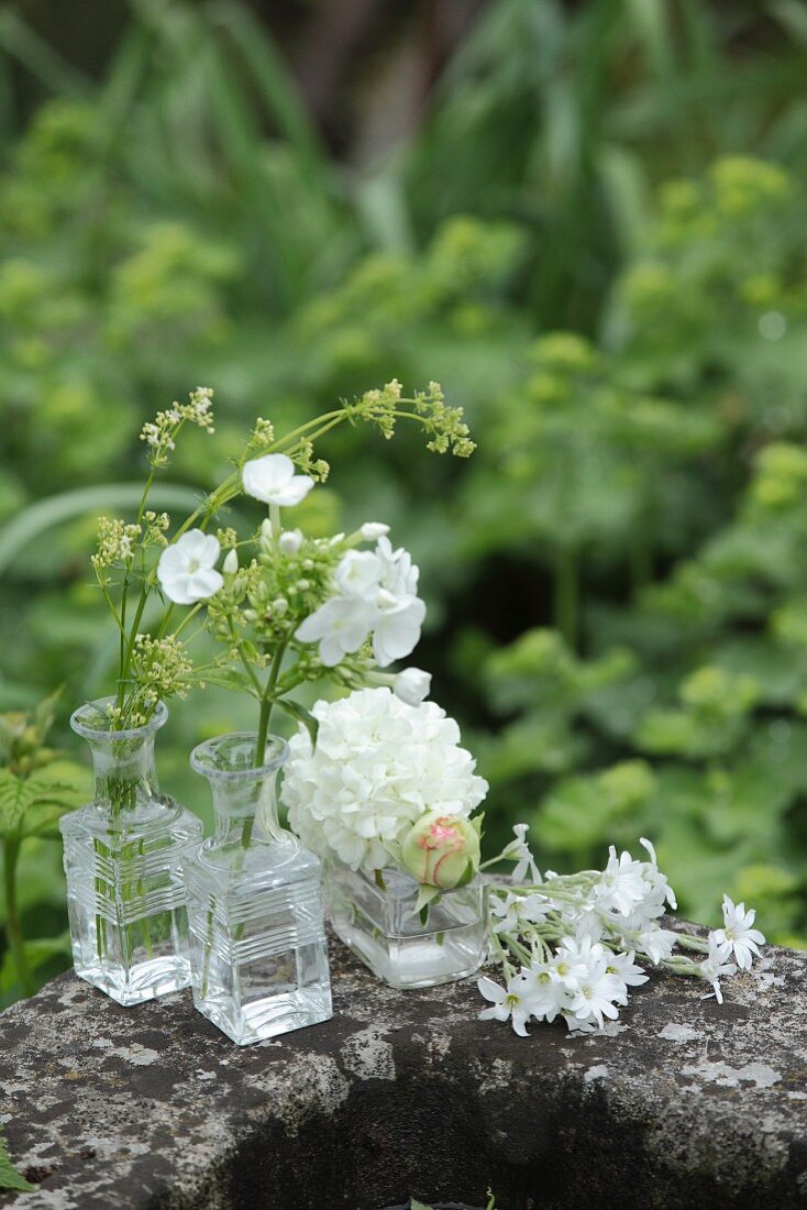 Verschiedene weiße Blumen in Glasväschen auf einem Steintrog