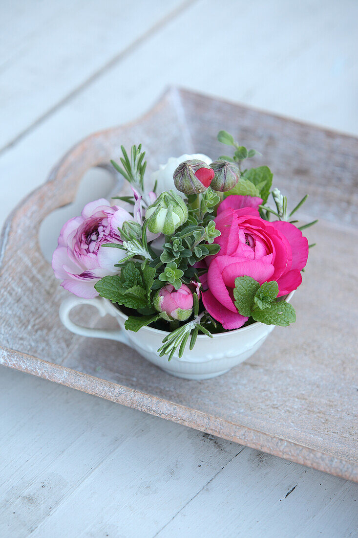 Romantic arrangement of ranunculus in coffee cup on wooden tray