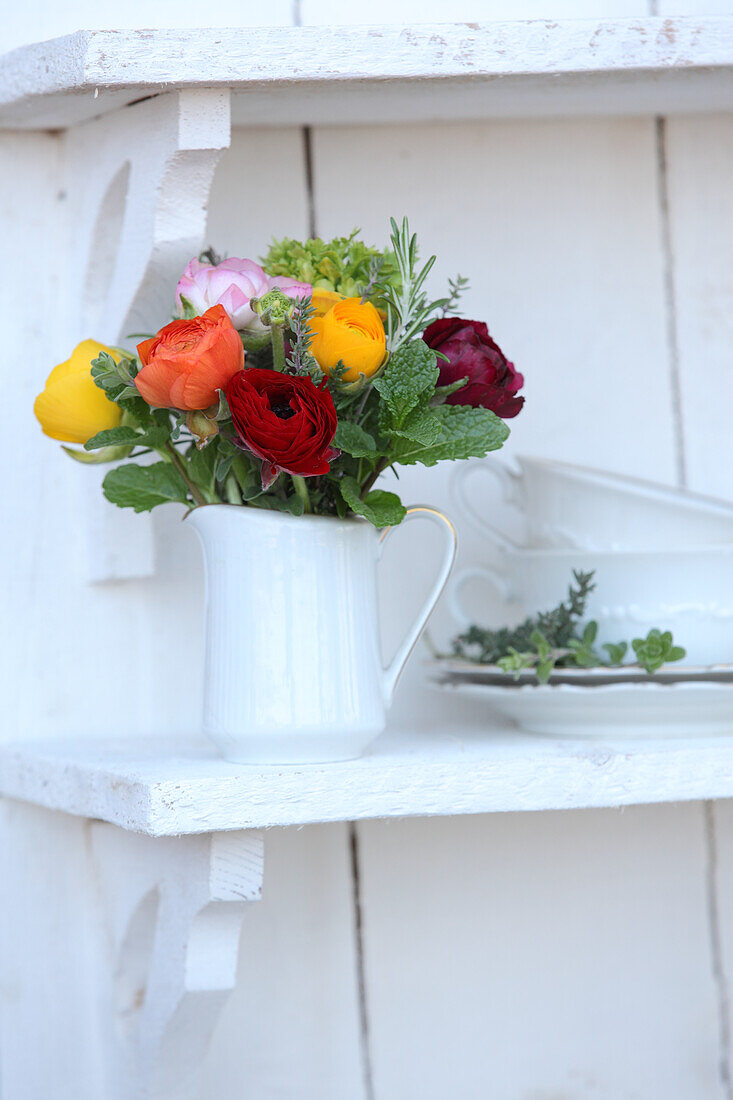 Bunch of colourful ranunculus in white jug on bracket shelf