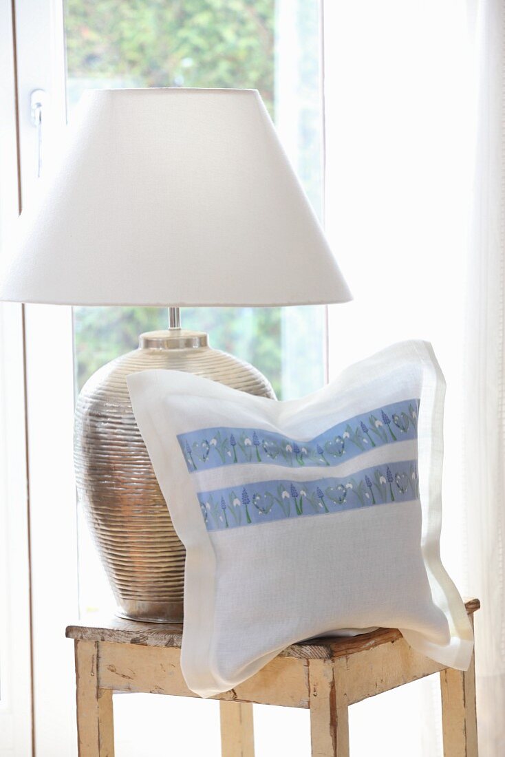 Cushion cover hand made from white linen and floral trim next to table lamp on wooden stool