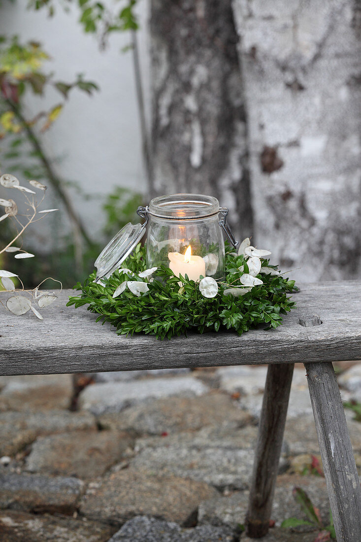 Lit candle in mason jar in wreath of box and honesty