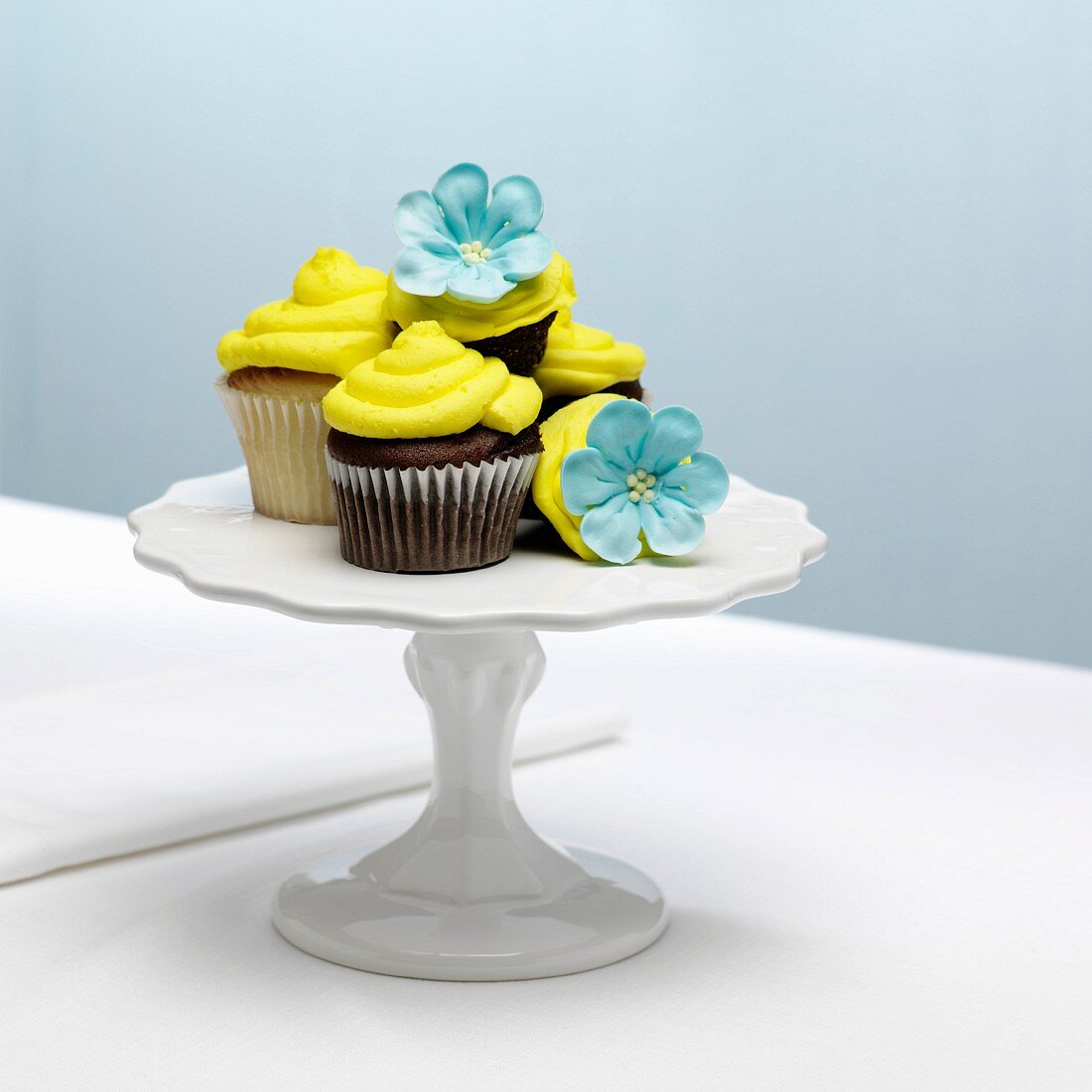 Schokoladen-und Vanille-Cupcakes mit gelbem Frosting und Zuckerblüten auf Kuchenständer