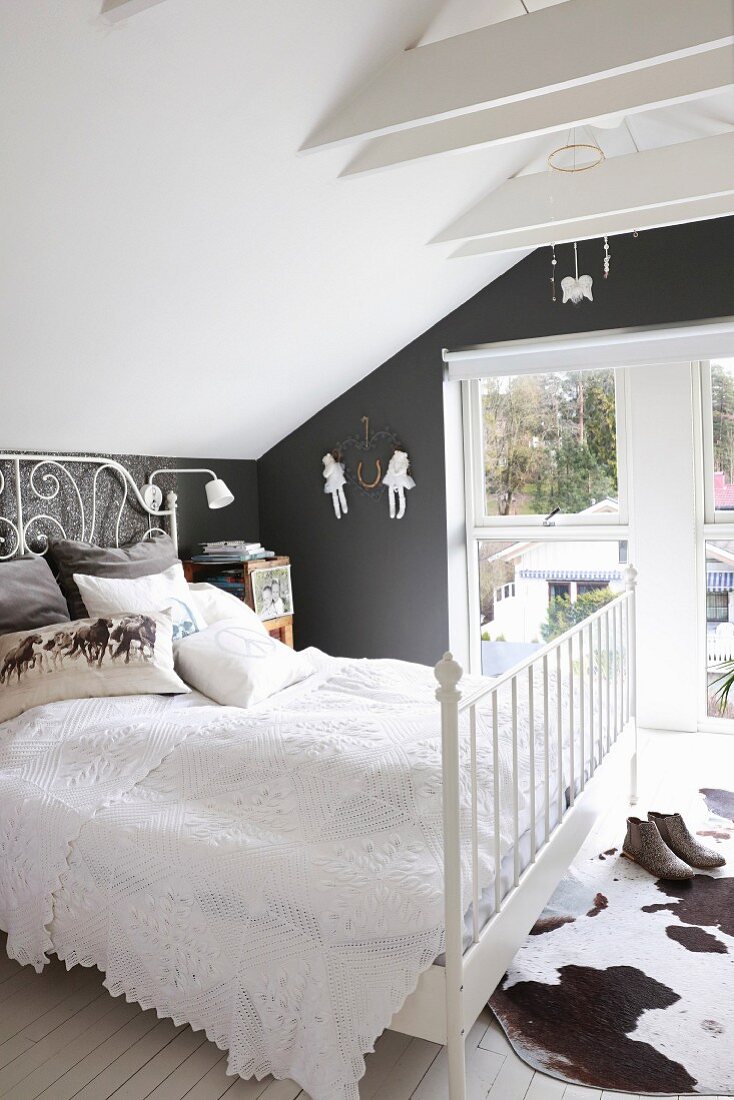 White blanket on bed and cowhide rug in attic room