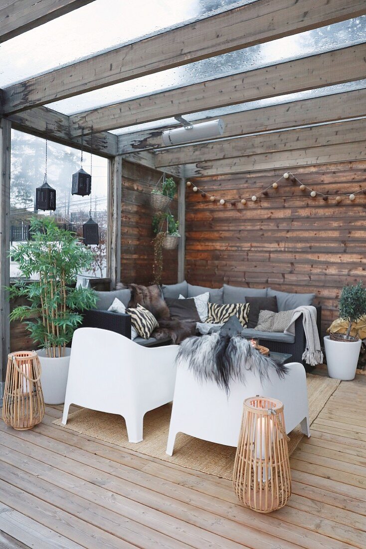 Gemütlicher Loungebereich auf überdachter Holzterrasse mit weißen Outdoorsesseln