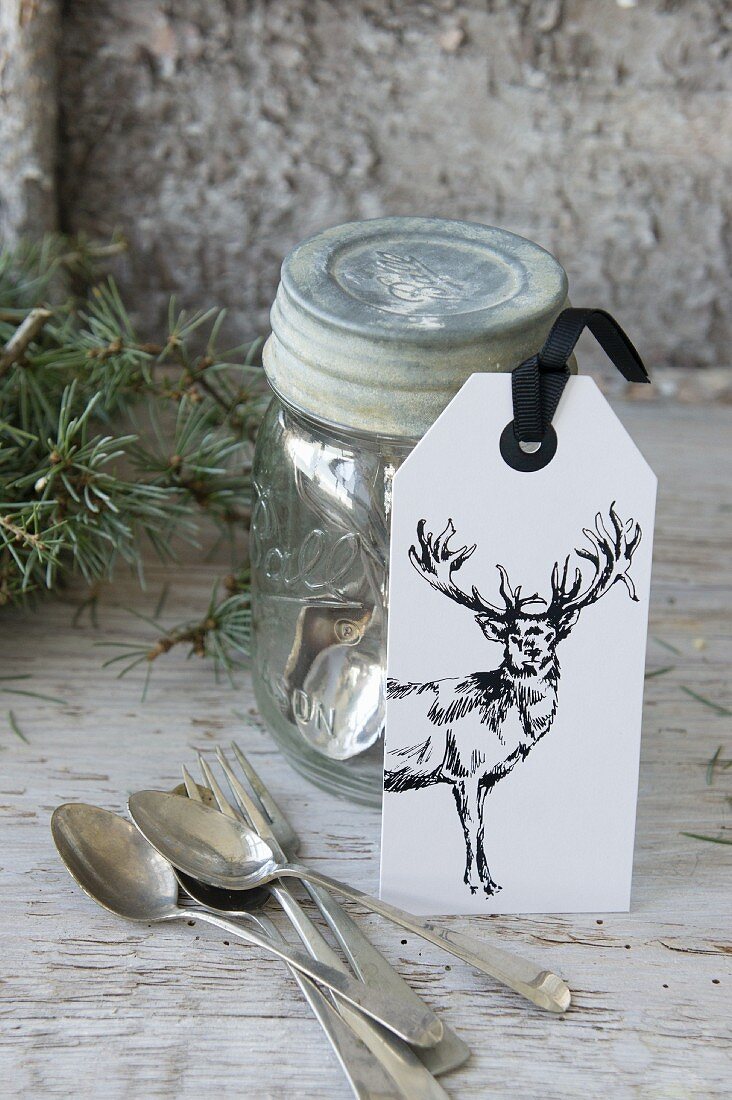 Etikett mit einem Hirsch lehnt am Einmachglas mit Silberbesteck