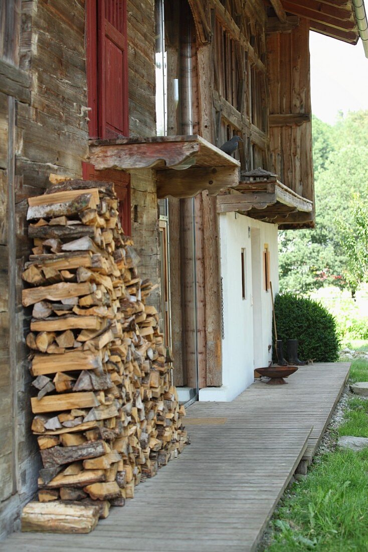 Brennholzstapel vor verwitterter Holzfassade