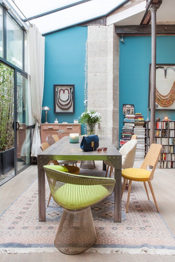 Esstisch mit verschiedenen Stühlen unterm Glasanbau vor blauer Wand