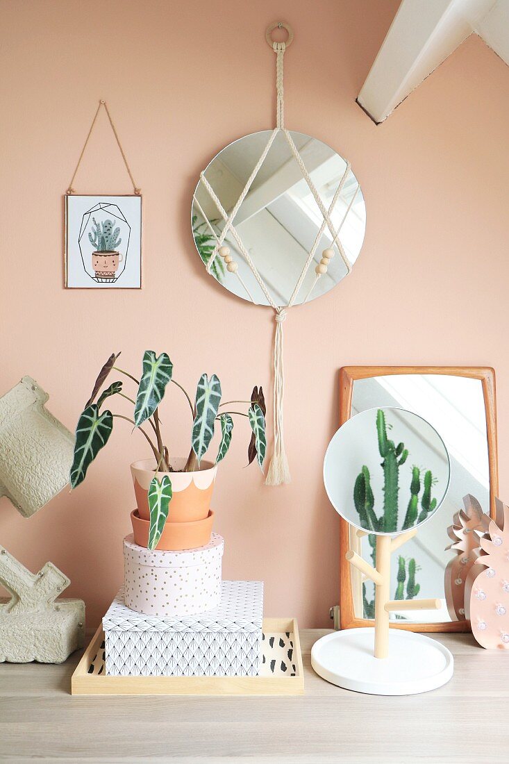 Wandspiegel mit Makramee und Holzperlen an apricotfarbener Wand, davor Zimmerpflanzen