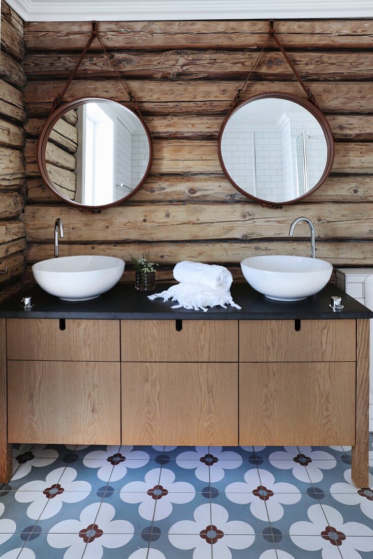 Massgefertigter Waschtisch mit zwei weissen Waschschüsseln vor rustikaler Holzbohlenwand und aufgehängten runden Spiegeln