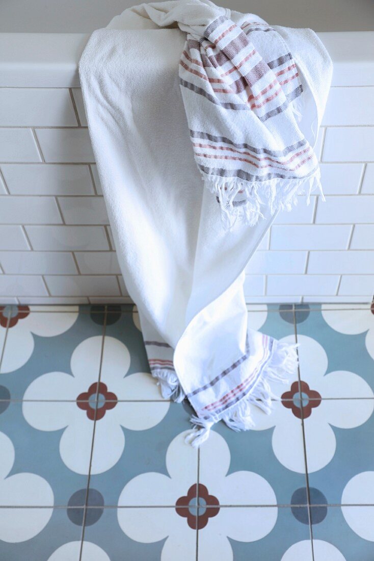 Handtuch auf Badewannenrand vor graublaue Zementbodenfliesen