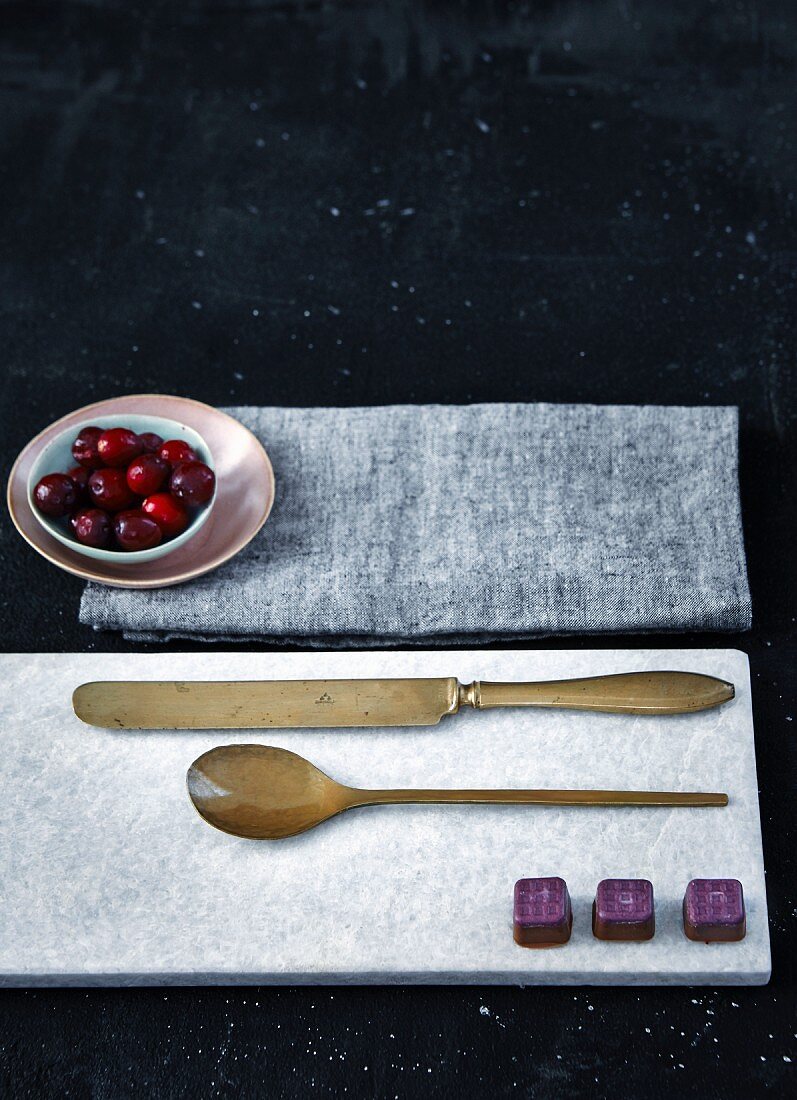 Schokoladenkonfekt auf Marmorbrett mit Besteck, Cranberries im Schälchen auf Tuch